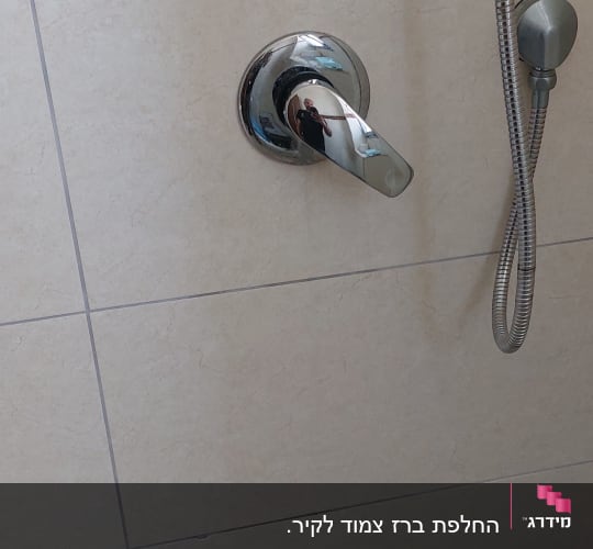 ברז מקלחת עם צינור מתכת על קיר אריחים